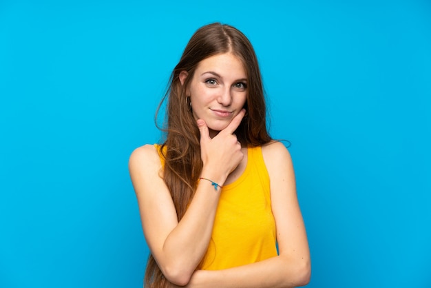 Young woman with long hair over isolated blue wall thinking