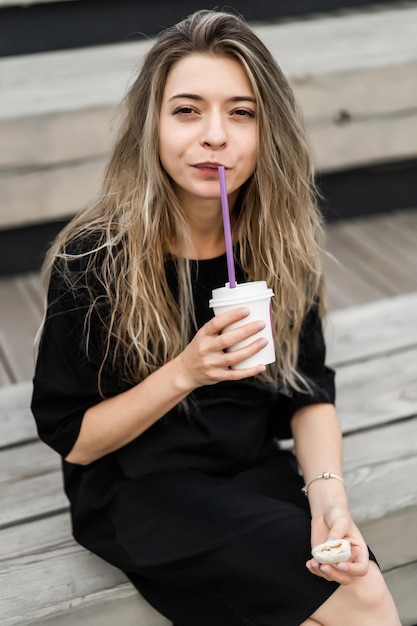 young woman with long hair outside. The girl drinks coffee from a cardboard cup.