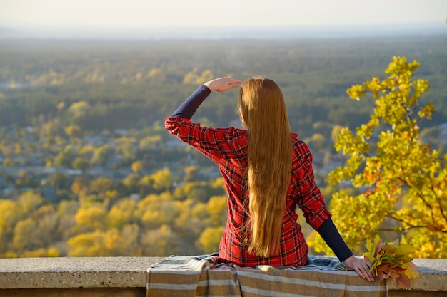 Young woman with long hair sits on a hill overlooking the city. 