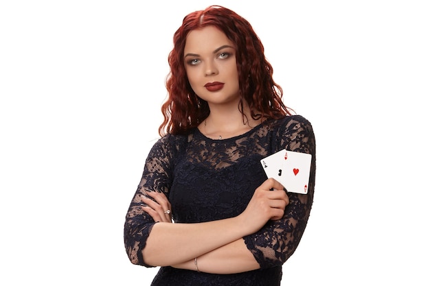 Young woman with a long red hair in evening outfit holding playing cards isolated on white poker