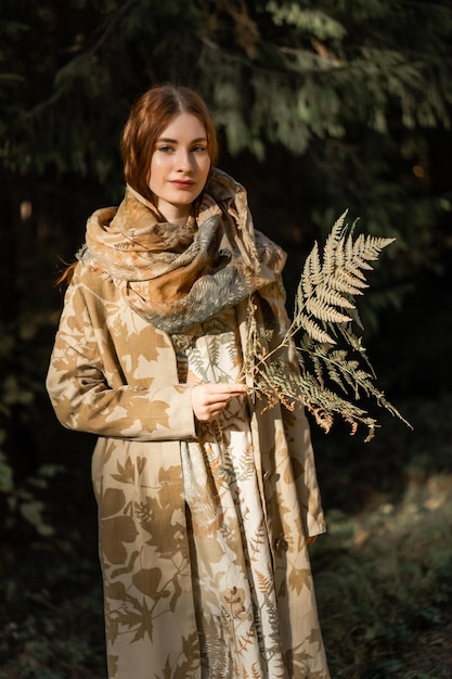 Photo young woman with long red hair in a linen dress gathering mushrooms in the forest in the bast basket