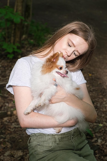 Young woman with long straight hair and fluffy small dog for walk in forest