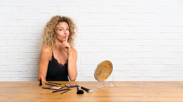 Young woman with lots of makeup brush in a table doing silence gesture