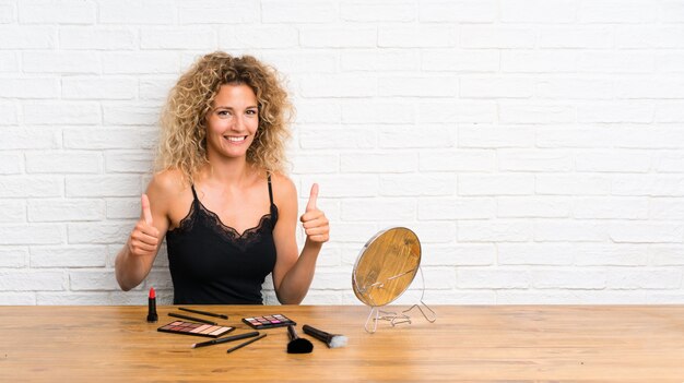 Young woman with lots of makeup brush in a table giving a thumbs up gesture