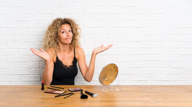 Photo young woman with lots of makeup brush in a table having doubts with confuse face expression