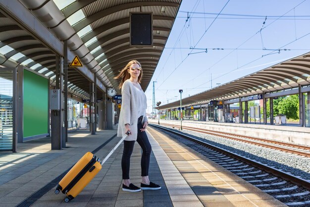 Young woman with luggage standing at railroad station