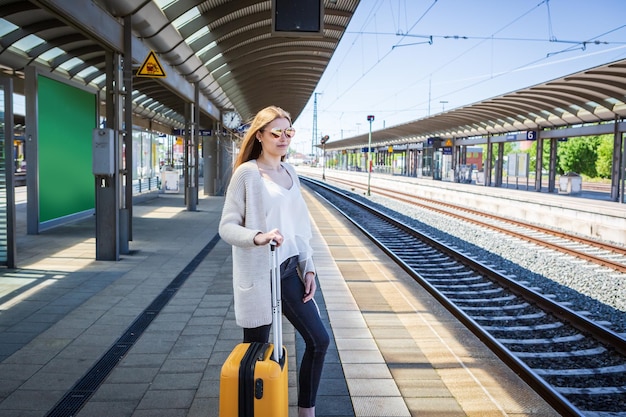鉄道駅のプラットフォームで荷物を待っている若い女性