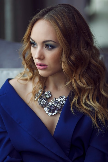 Young woman with makeup in a blue suit, wear silver necklace, in natural light