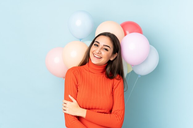 Young woman with many balloons isolated on blue wall