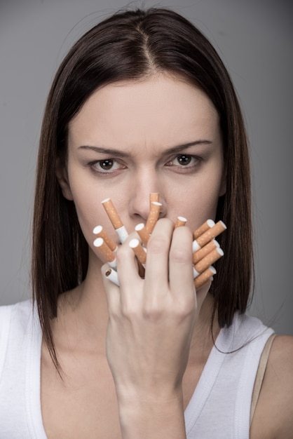 Foto giovane donna con molte sigarette in bocca.