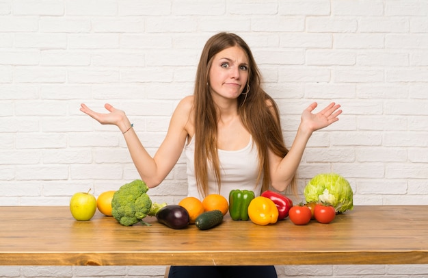 Young woman with many vegetables having doubts with confuse face expression