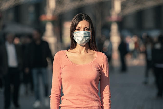 The young woman with medical mask on her face stands on the urban street