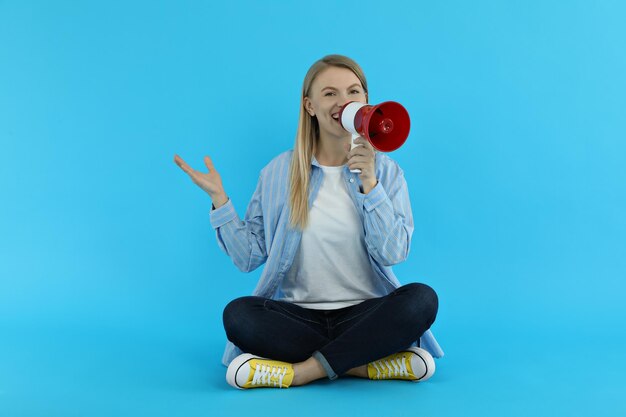 Young woman with megaphone on blue background