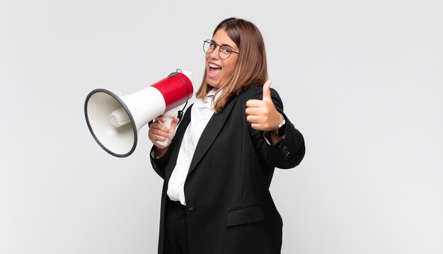 Photo young woman with a megaphone feeling proud, carefree, confident and happy, smiling positively with thumbs up