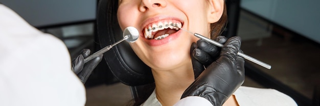 A young woman with metal braces is being examined by an orthodontist correction of the bite of teeth