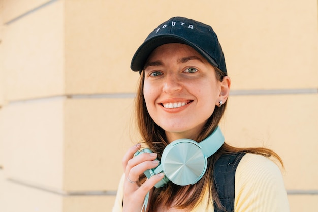 Young woman with mint headphones and black cap outside on the street