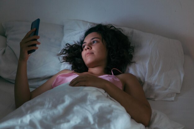 Young woman with mobile phone in bed at night internet addiction