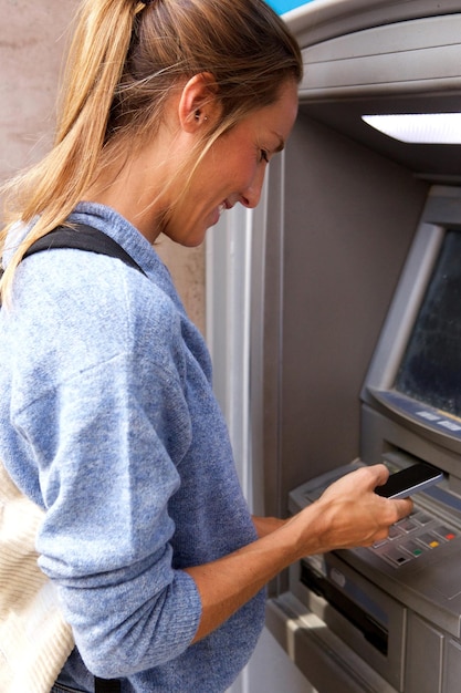 Young woman with mobile phone by bank machine