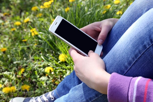 Young woman with mobile phone sitting on green grass outdoors