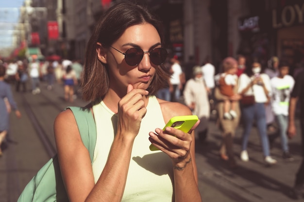 Молодая женщина с мобильным телефоном путешествует по многолюдным улицам стамбула, счастливая, наслаждаясь красотой города
