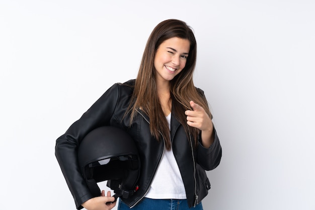 Молодая женщина с мотоциклетным шлемом над белой стеной показывает пальцем на тебя