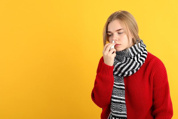 Young woman with nasal drops on yellow background, runny nose concept