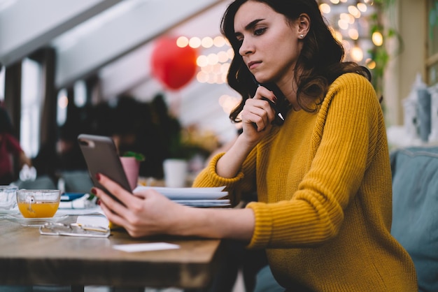 Young woman with notebook on desk using smartphone