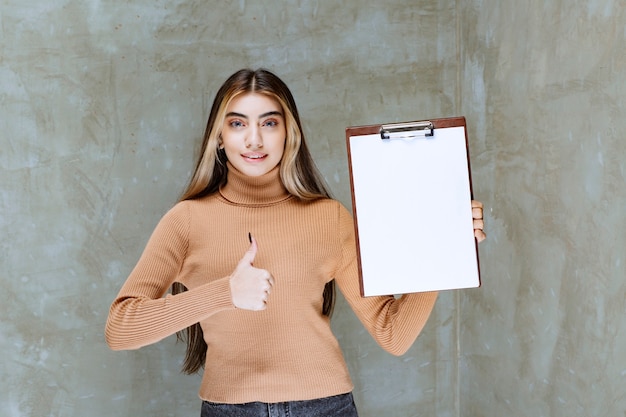 石の上に親指を示すメモ帳を持つ若い女性