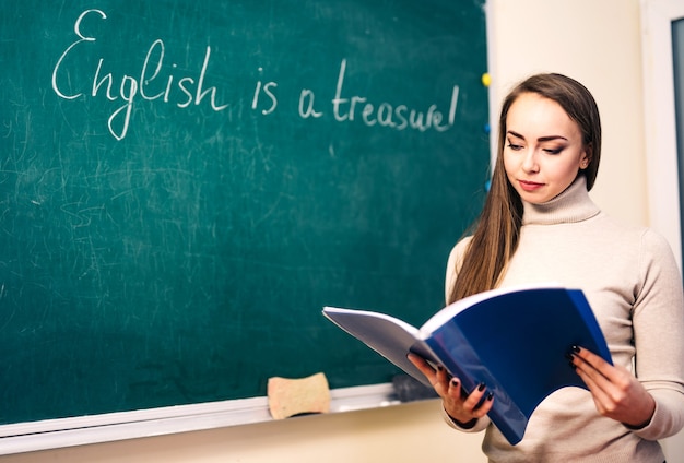 Young woman with notes is standing near the blackboard