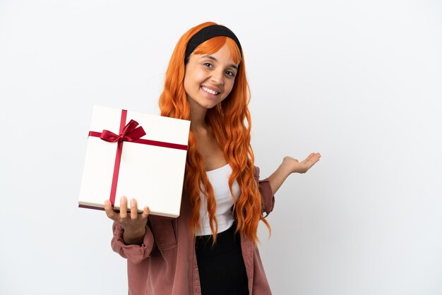 Young woman with orange hair holding a gift isolated on white background extending hands to the side for inviting to come