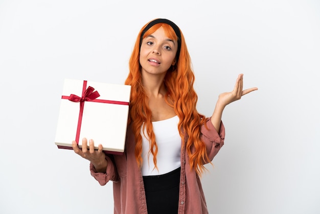 Young woman with orange hair holding a gift isolated on white background extending hands to the side for inviting to come