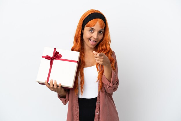 Young woman with orange hair holding a gift isolated on white background pointing front with happy expression