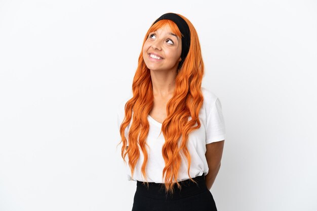 Молодая женщина с оранжевыми волосами на белом фоне думает об идее, глядя вверх