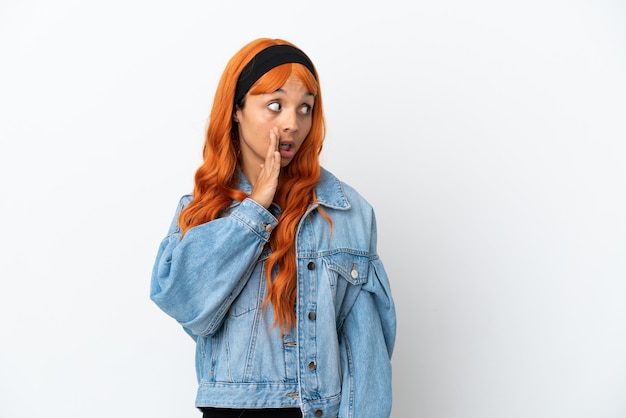 Young woman with orange hair isolated on white background whispering something with surprise gesture while looking to the side