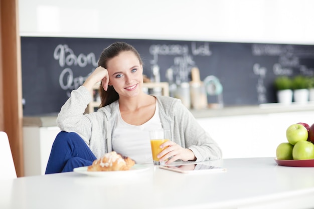 Young woman with orange juice and tablet in kitchen