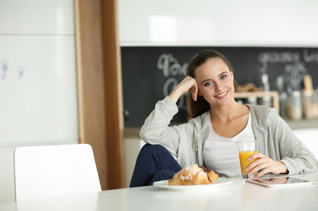 キッチンでオレンジジュースとタブレットを持つ若い女性