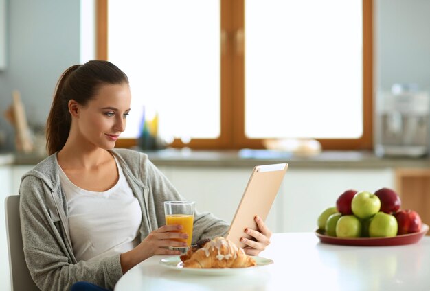 キッチンでオレンジジュースとタブレットを持つ若い女性