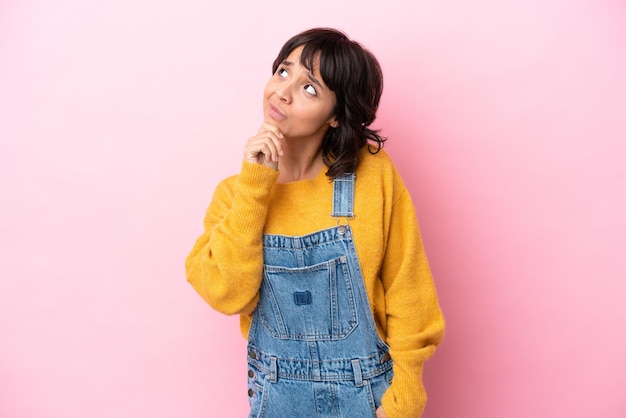 Young woman with overalls isolated background having doubts