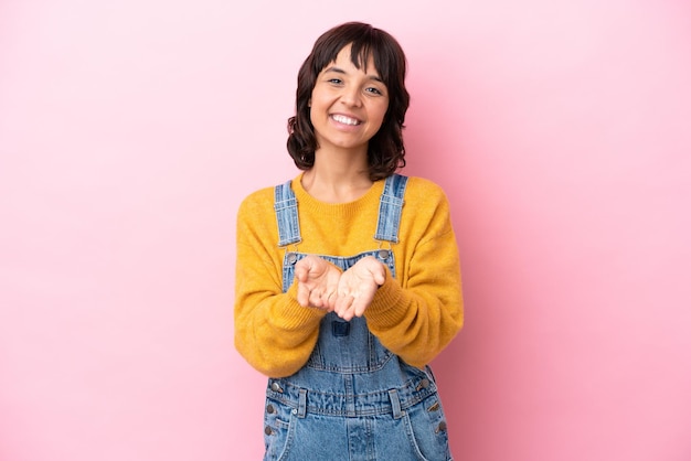 Young woman with overalls isolated background holding copyspace imaginary on the palm to insert an ad