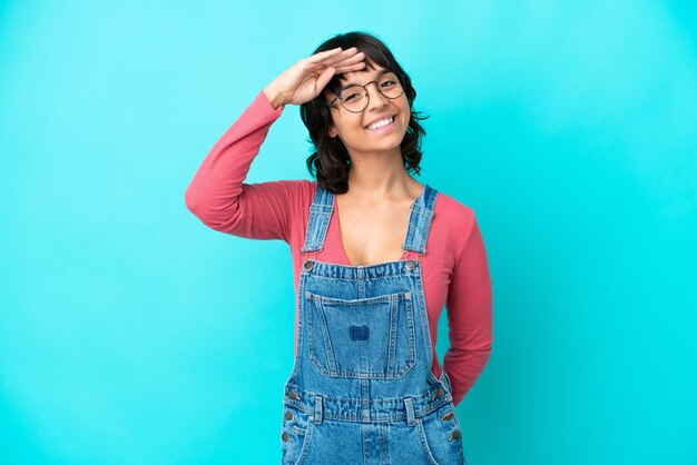 Young woman with overalls isolated background saluting with hand with happy expression