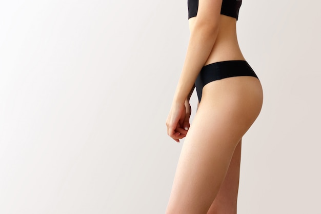 Young woman with perfect body on grey wall. Cellulite problem concept. Liposuction. Beautiful female hips