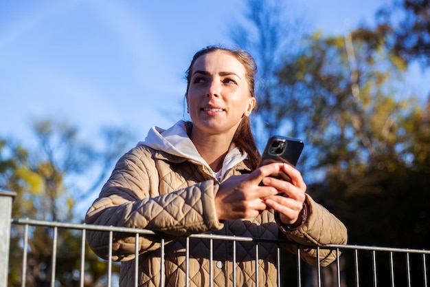 Young woman with a phone looks away on the background of an autumn park