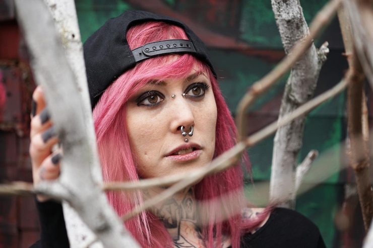 Photo young woman with pierced face and tattooed neck behind tree branches