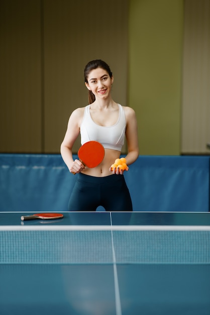 Young woman with ping pong racket and  ball at the table indoors.