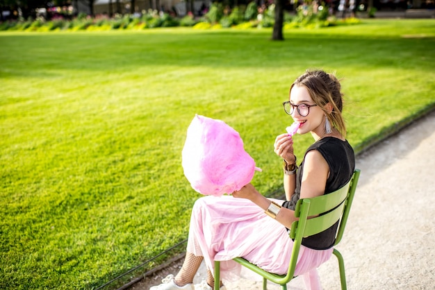 公園で屋外に座っているピンクの綿菓子を持つ若い女性