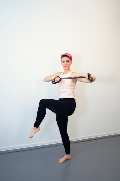 Young woman with pink hair does a back exercise with a rubber shock absorber