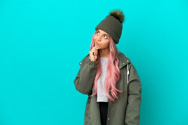 Young woman with pink hair wearing a rainproof coat isolated on blue background and looking up