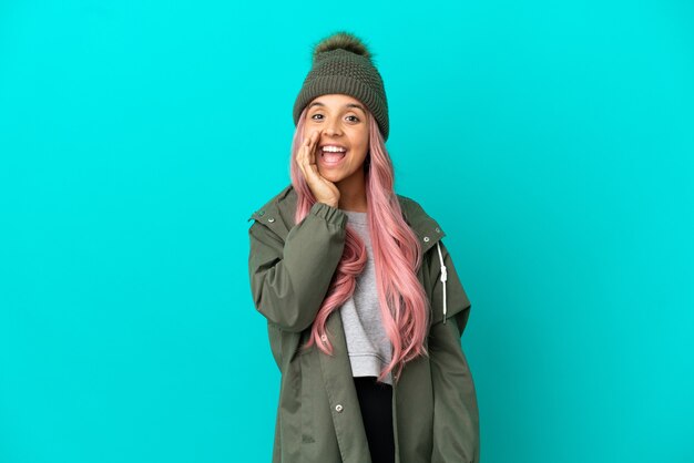 Young woman with pink hair wearing a rainproof coat isolated on blue background shouting with mouth wide open