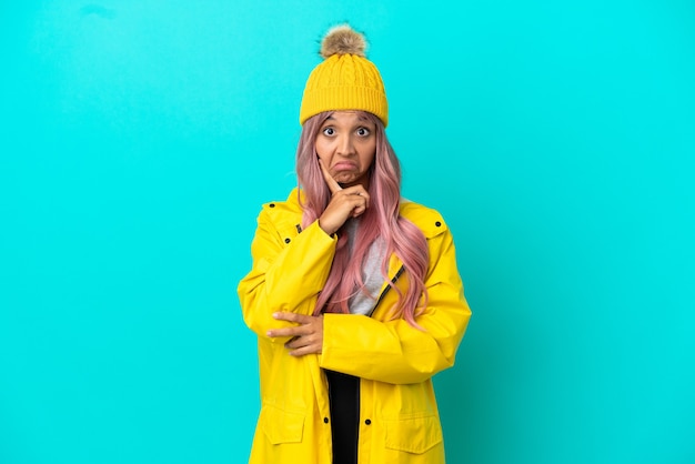 Young woman with pink hair wearing a rainproof coat isolated on blue background and thinking