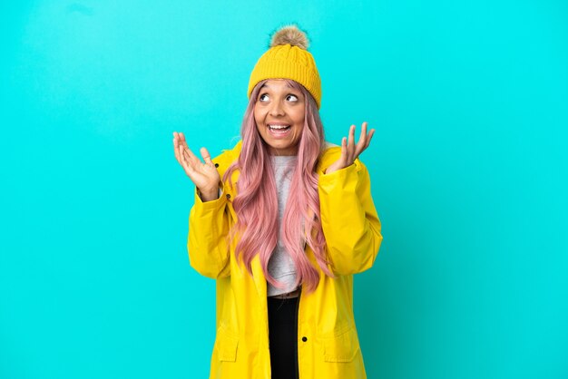 Young woman with pink hair wearing a rainproof coat isolated on blue background with surprise facial expression